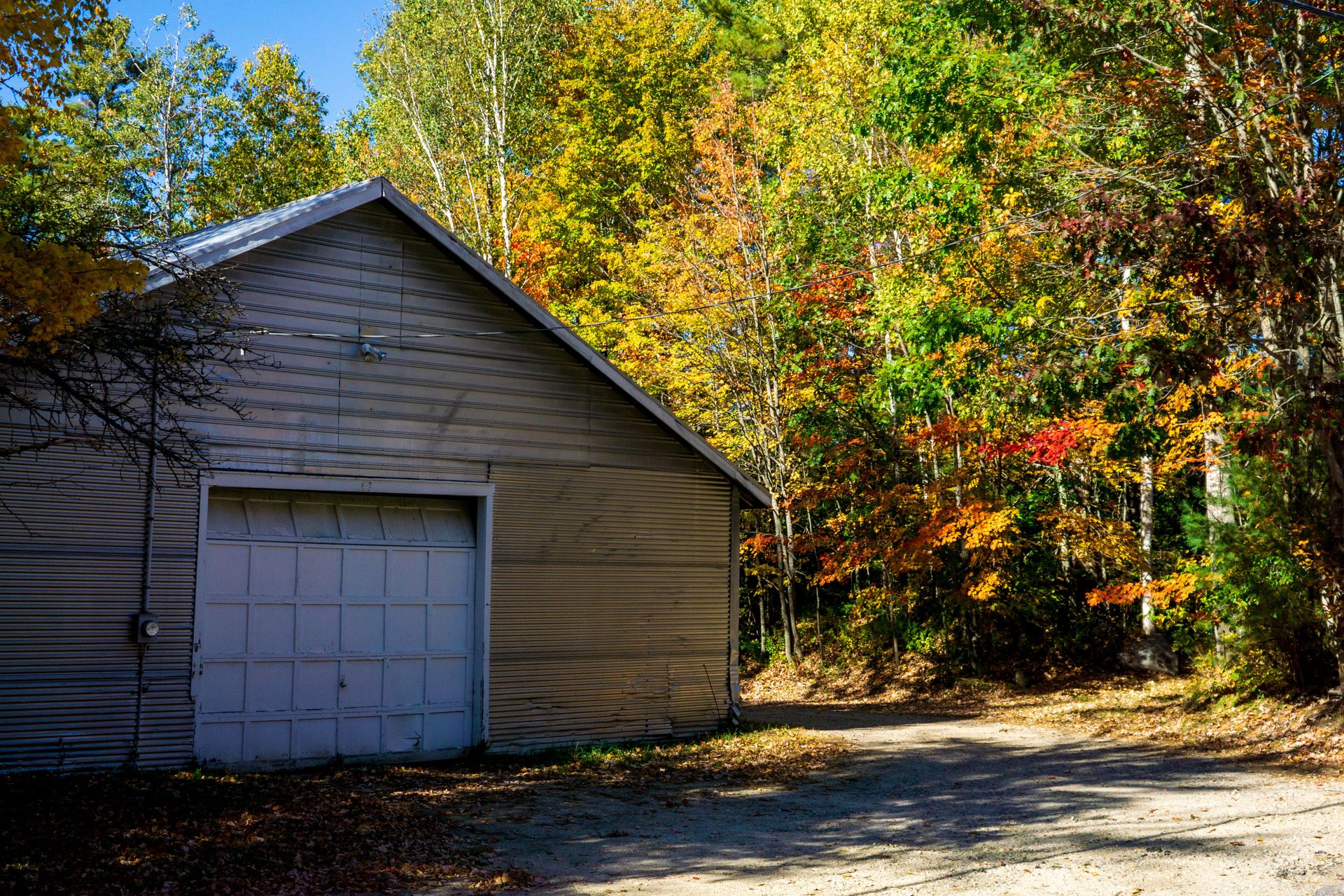 A metal barn surrounded by colorful autumn trees on a sunny day, showcasing the beauty of fall foliage.