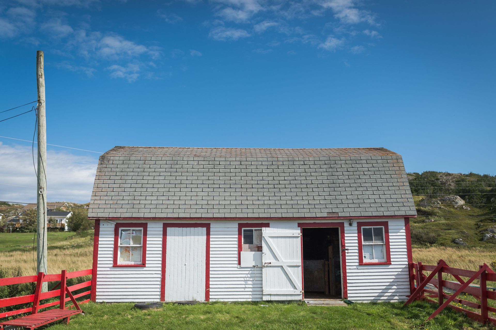 Charming red and white barn situated in a serene rural landscape under a bright blue sky.
